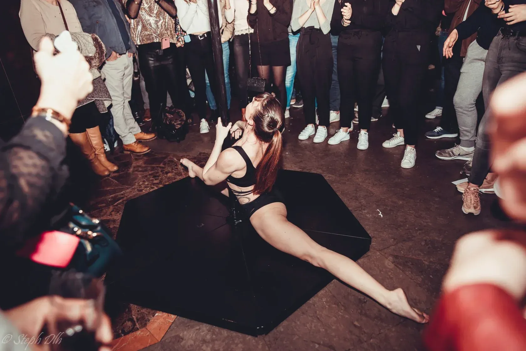 Une femme fait un grand écart sur le sol devant une foule de gens.
