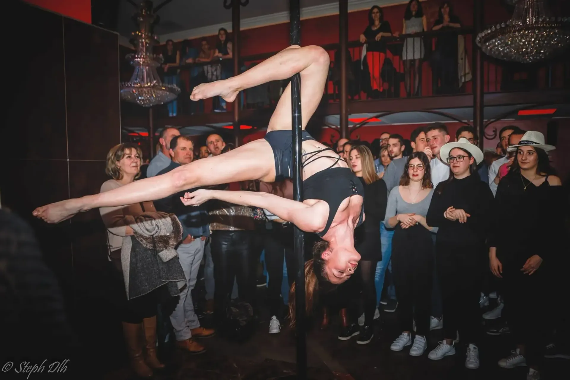 Une femme fait une pole dance devant une foule de gens.