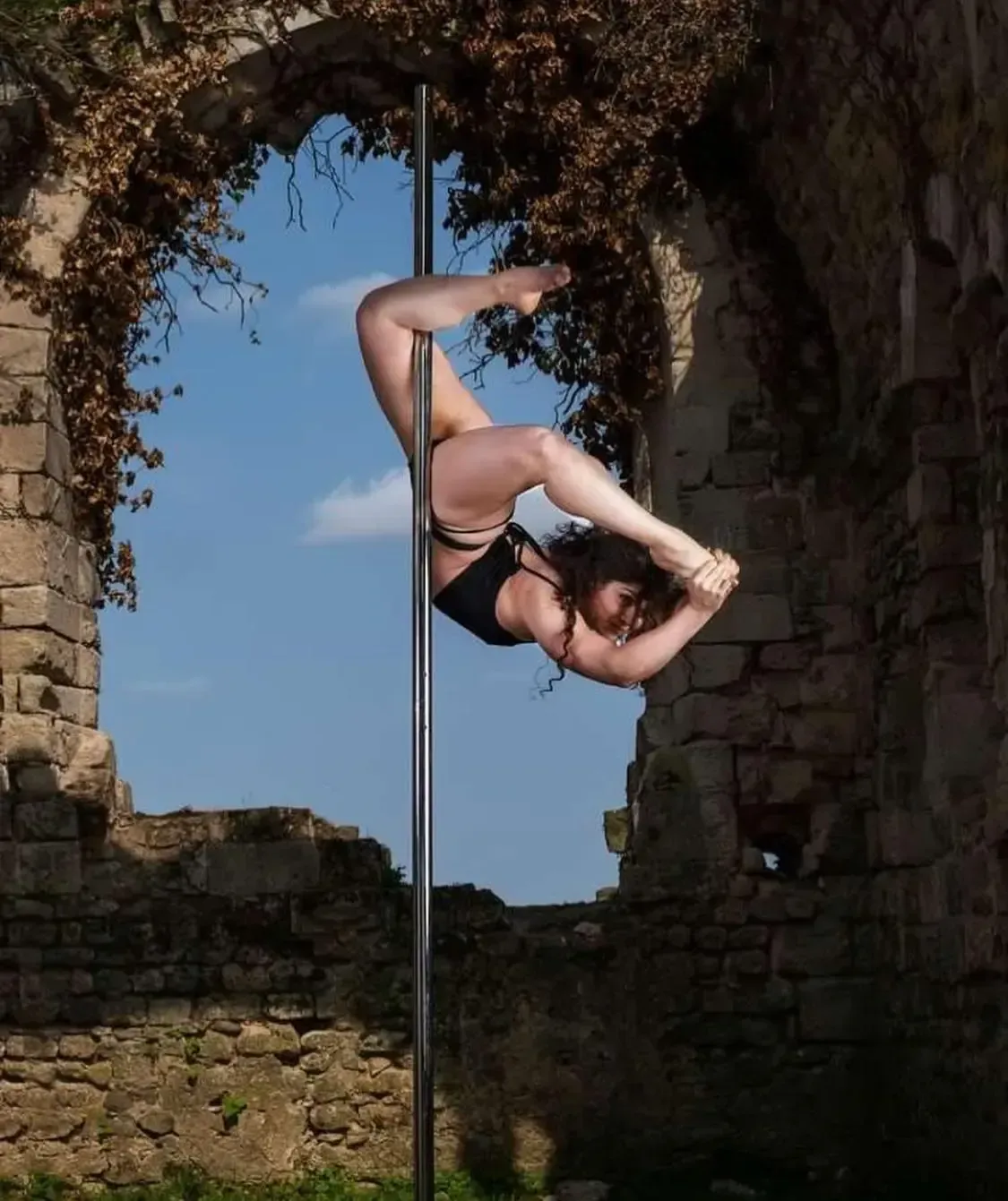 Une femme fait le poirier sur un poteau devant un mur de pierre