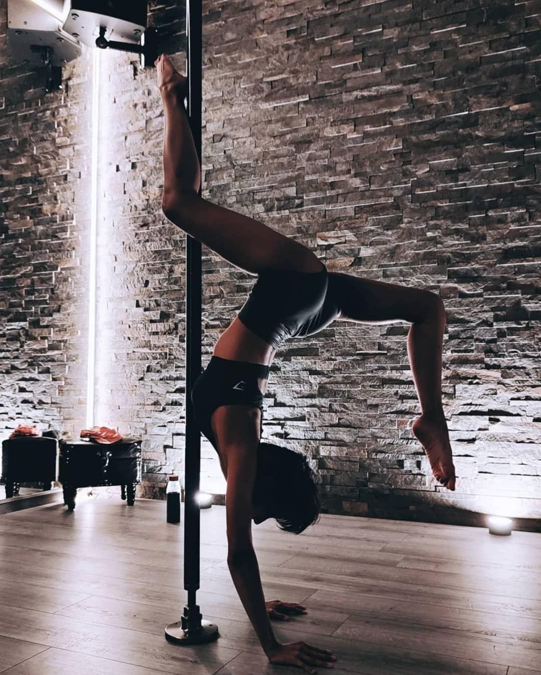Une femme fait le poirier sur un poteau dans une salle de sport.