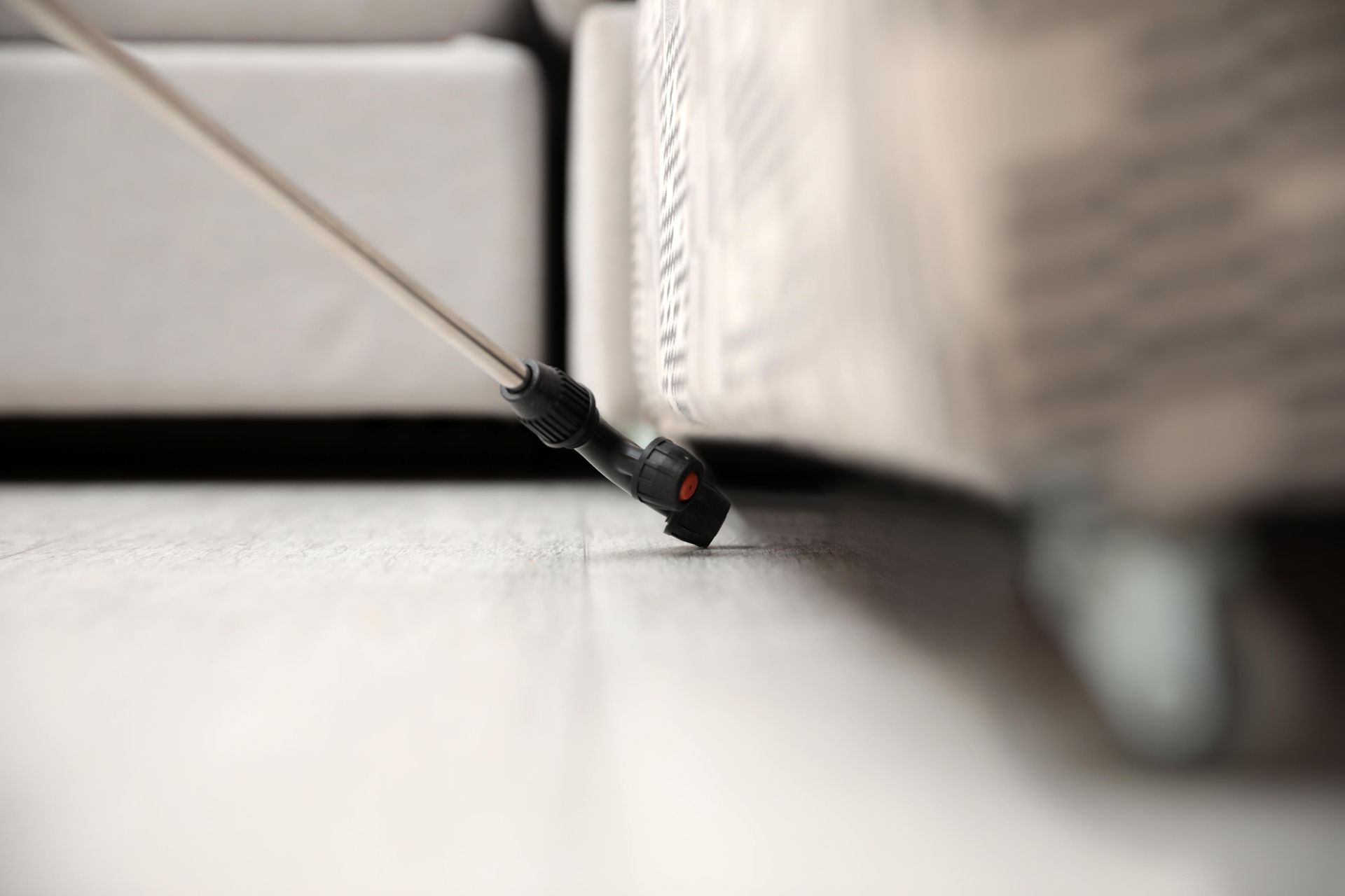 Pest control technician spraying insecticide near a piece of furniture's legs on a light-colored floor.