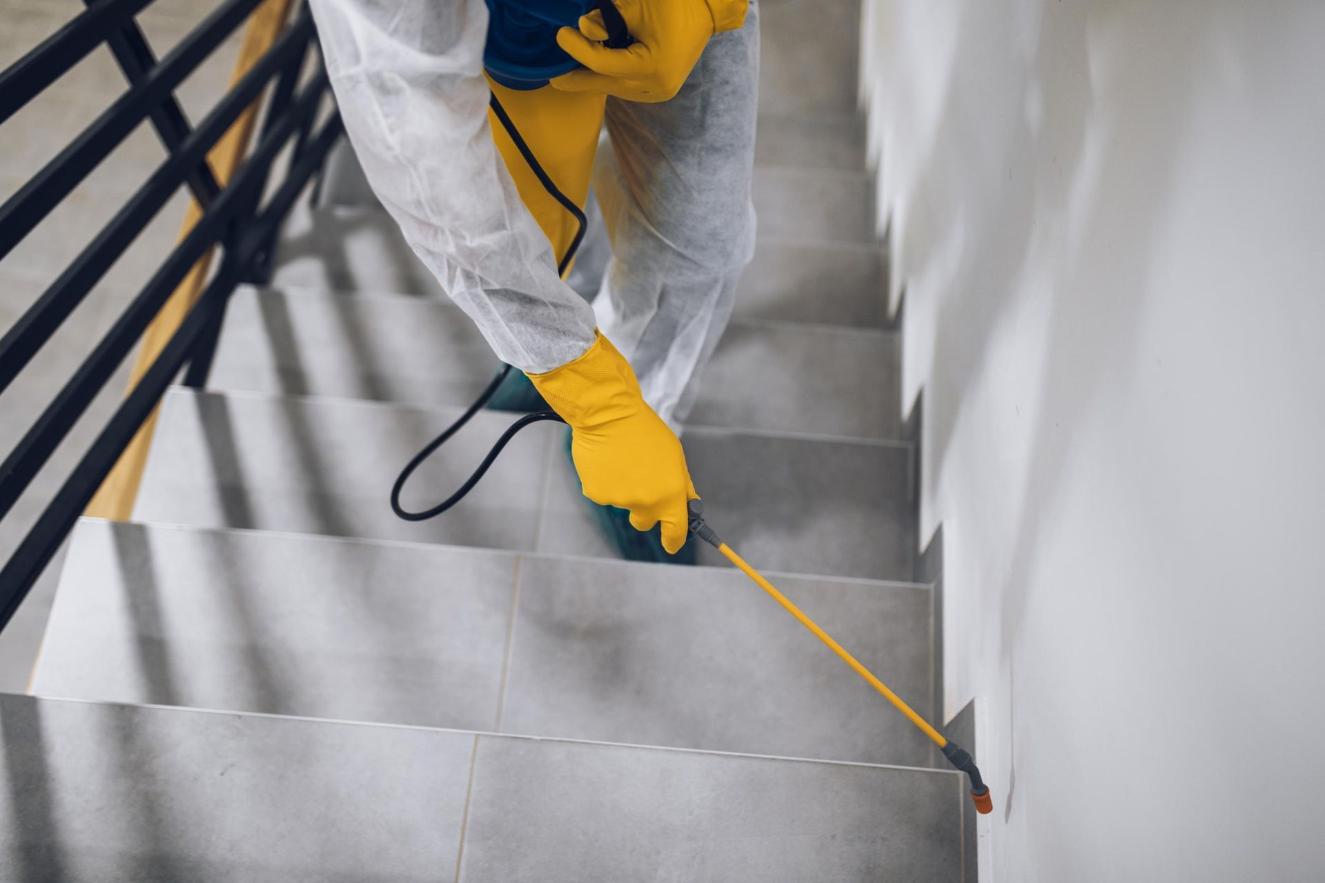 Person in protective suit spraying disinfectant on stairs.