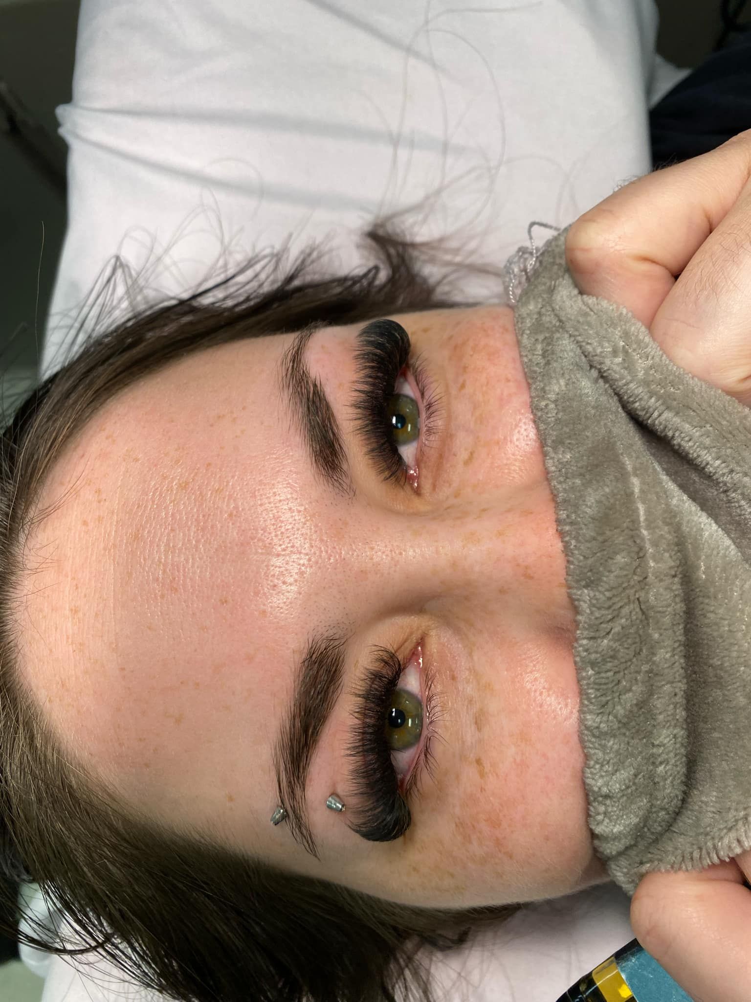 A woman is laying on a bed with a towel around her face.
