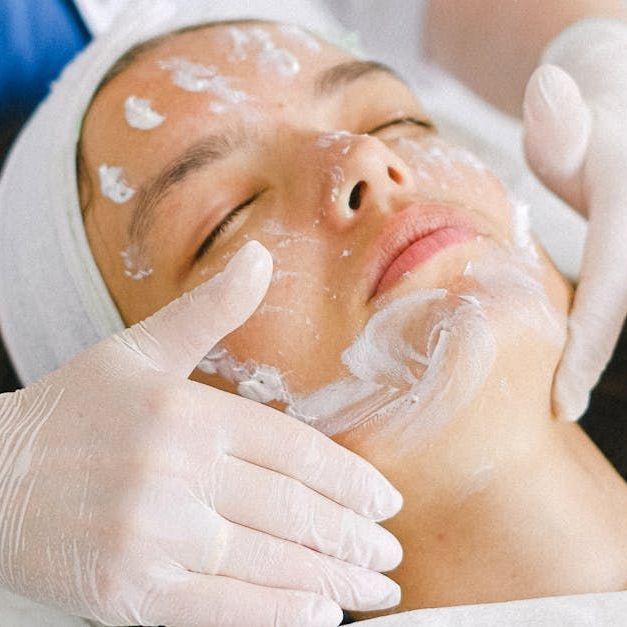 A woman is getting a facial treatment with gloves on her hands
