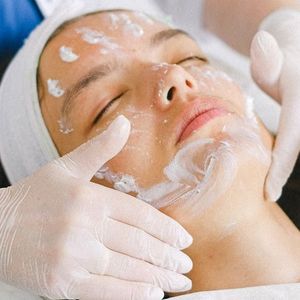 A woman is getting a facial treatment with gloves on her hands