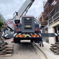 A large crane is parked on the side of the road next to a building.