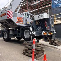A large crane is parked on the side of the road next to a pile of wooden pallets.