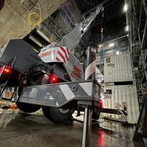 A large crane is parked in a warehouse next to shipping containers.