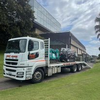 A white truck with a flatbed is parked in front of a building.