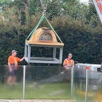 A crane is lifting a wooden pizza oven into the air.