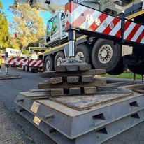 A crane is sitting on top of a stack of metal plates on the side of the road.