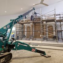 A green crane is parked in front of a building under construction.