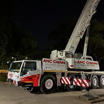 A large crane is parked in a parking lot at night.