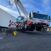 A large crane is parked in a parking lot next to a building.