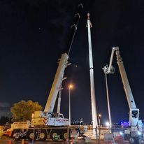 A couple of cranes are working on a pole at night.