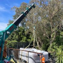 A crane is lifting a hot tub over a fence.