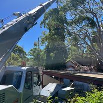 A truck with a crane attached to it is cutting a tree.