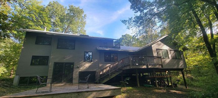 A large wooden house with a large deck in the middle of a forest.
