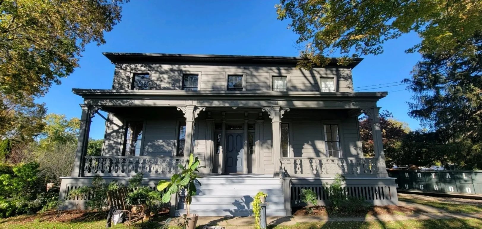 A large house with a porch is surrounded by trees on a sunny day.