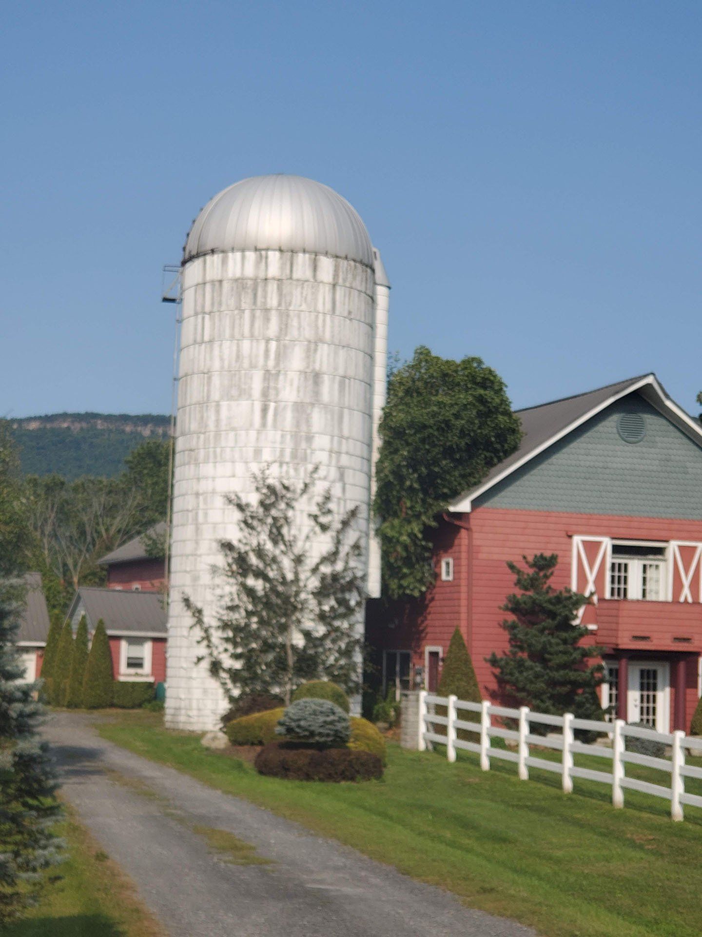 A large white silo sits in front of a red barn