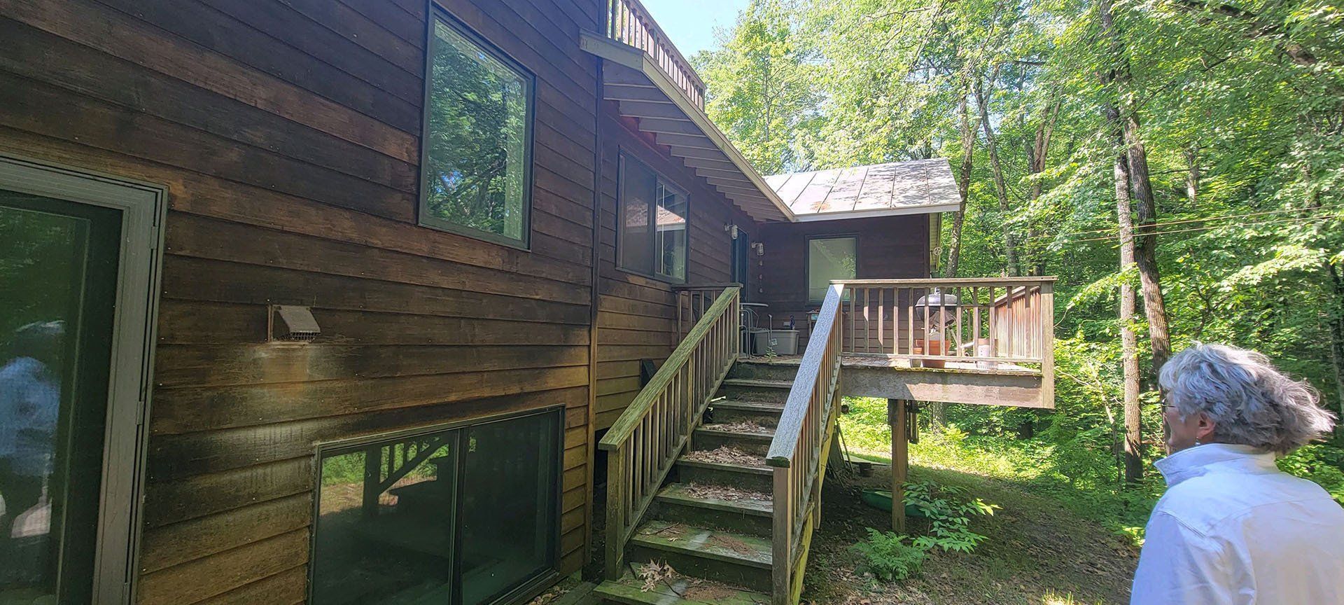 A man is standing in front of a wooden house with stairs leading up to it.