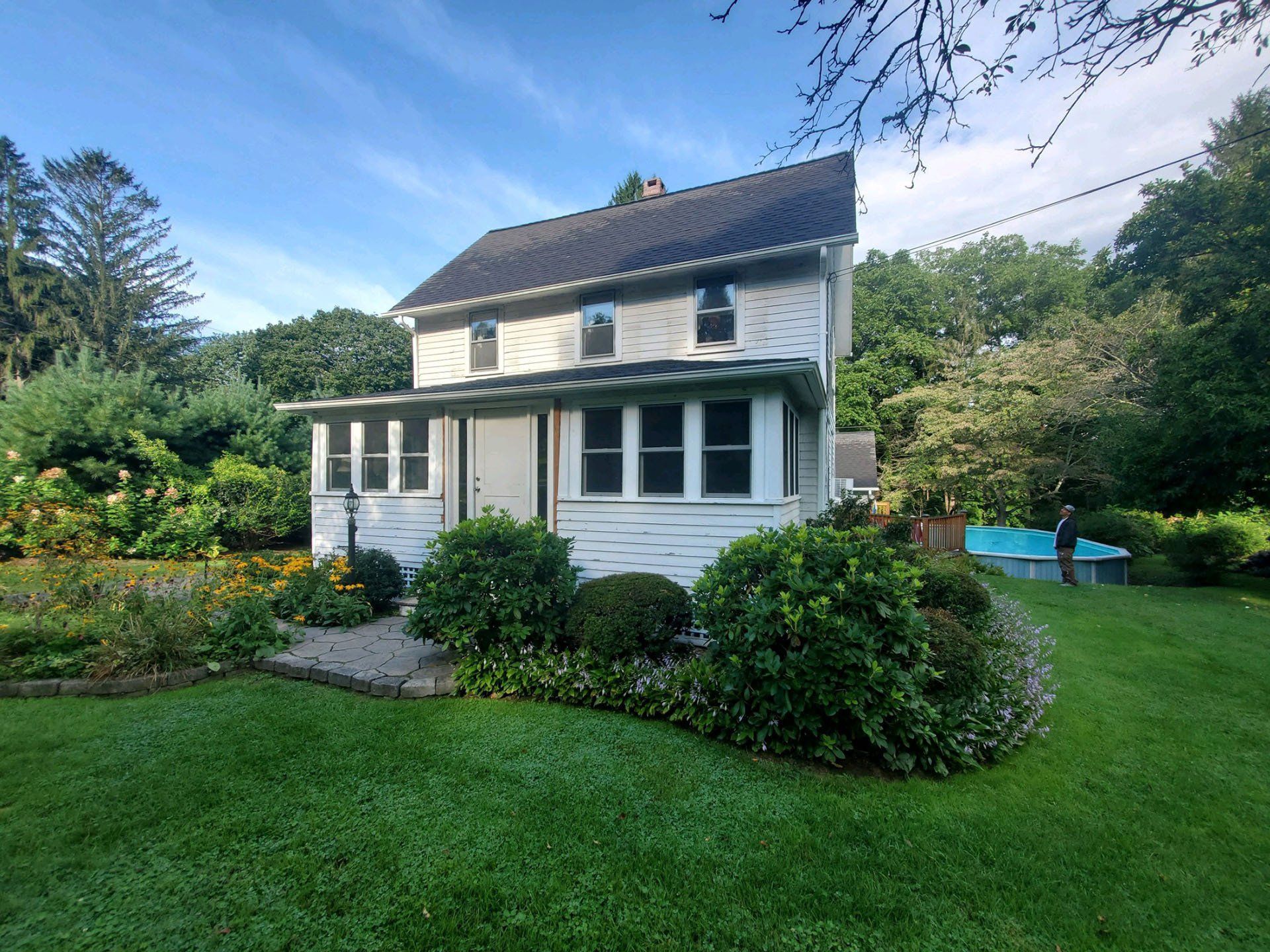 A white house with a black roof sits in the middle of a lush green yard