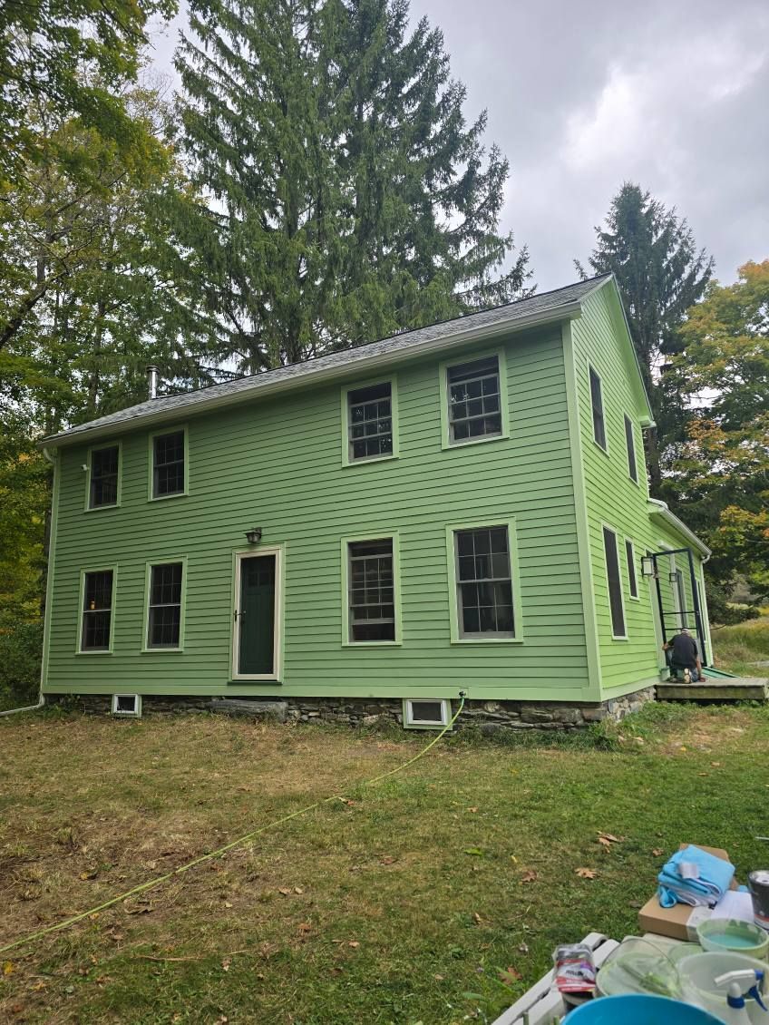 A large gray house with a white porch and a blue trash can in front of it.