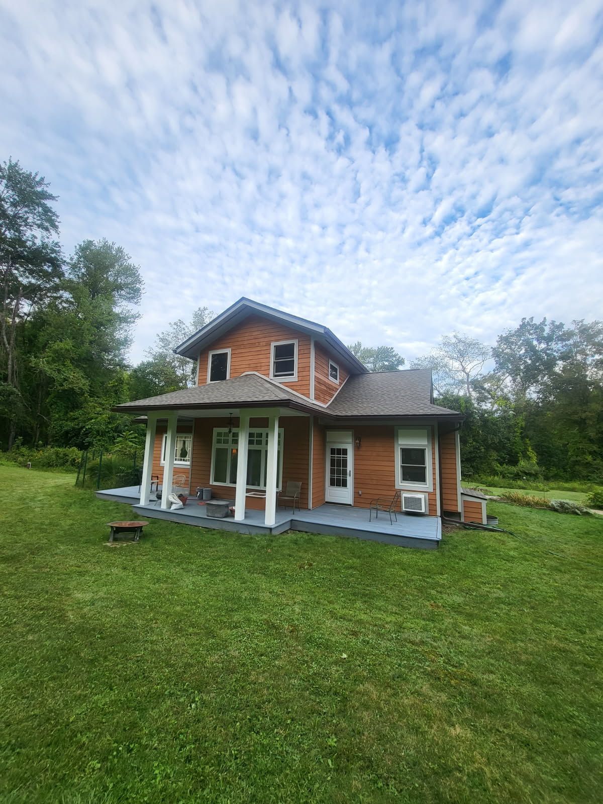 A brick house with a porch is sitting in the middle of a lush green field.