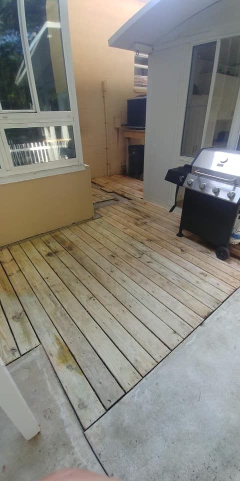 Wooden deck with a grill, next to a concrete patio, and the side of a house.