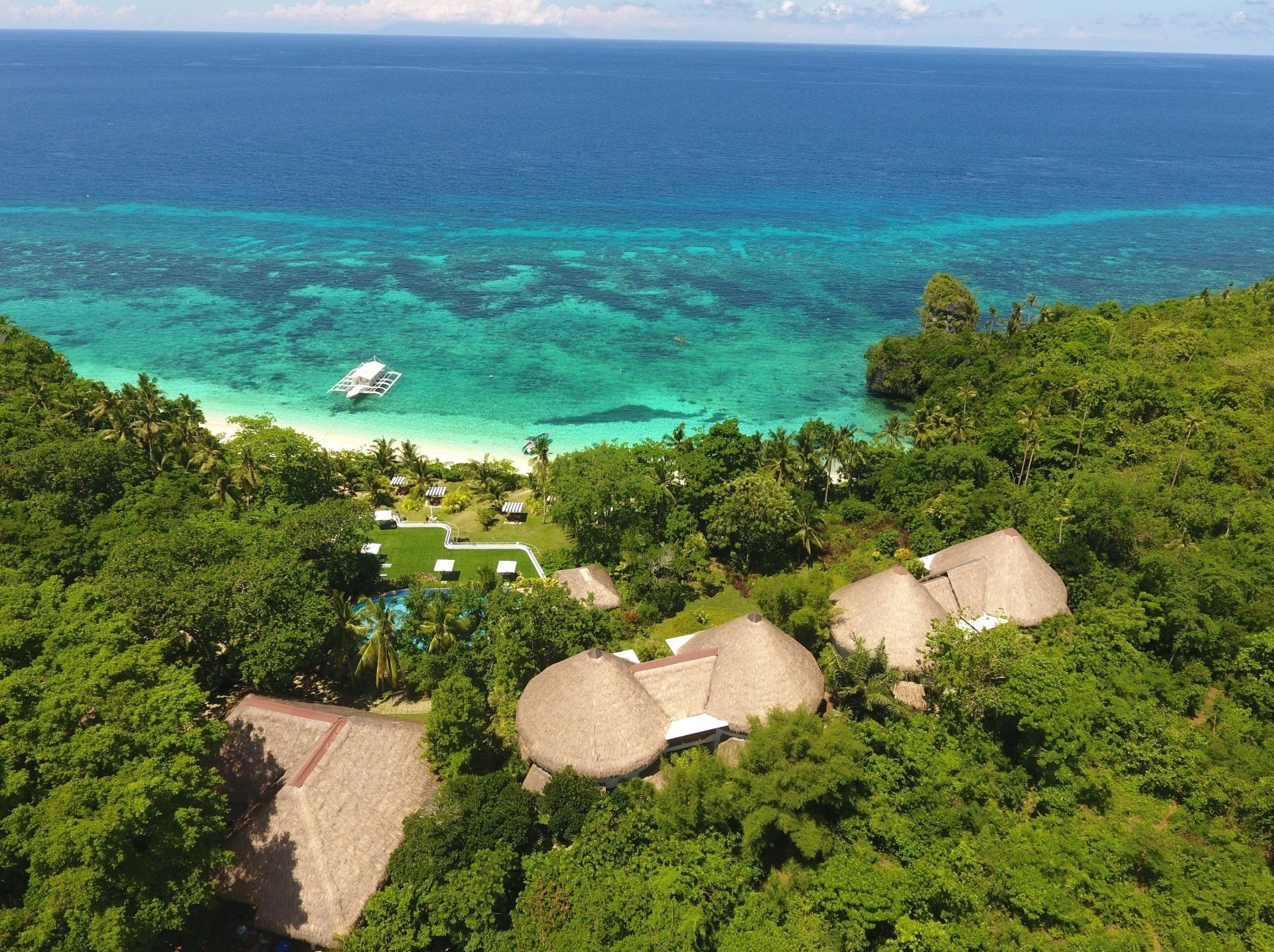 Aerial view of Amun Ini Beach Resort surrounded by lush greenery and crystal-clear sea.