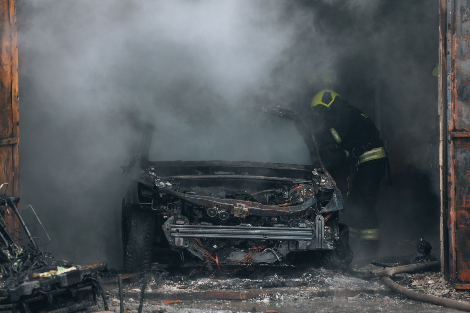 A firefighter stands beside a heavily damaged, smoke-filled car inside a building. A firefighter stands beside a heavily damaged, smoke-filled car inside a building.
