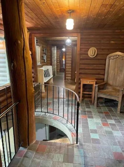 A hallway in a log cabin with a staircase and a chair.