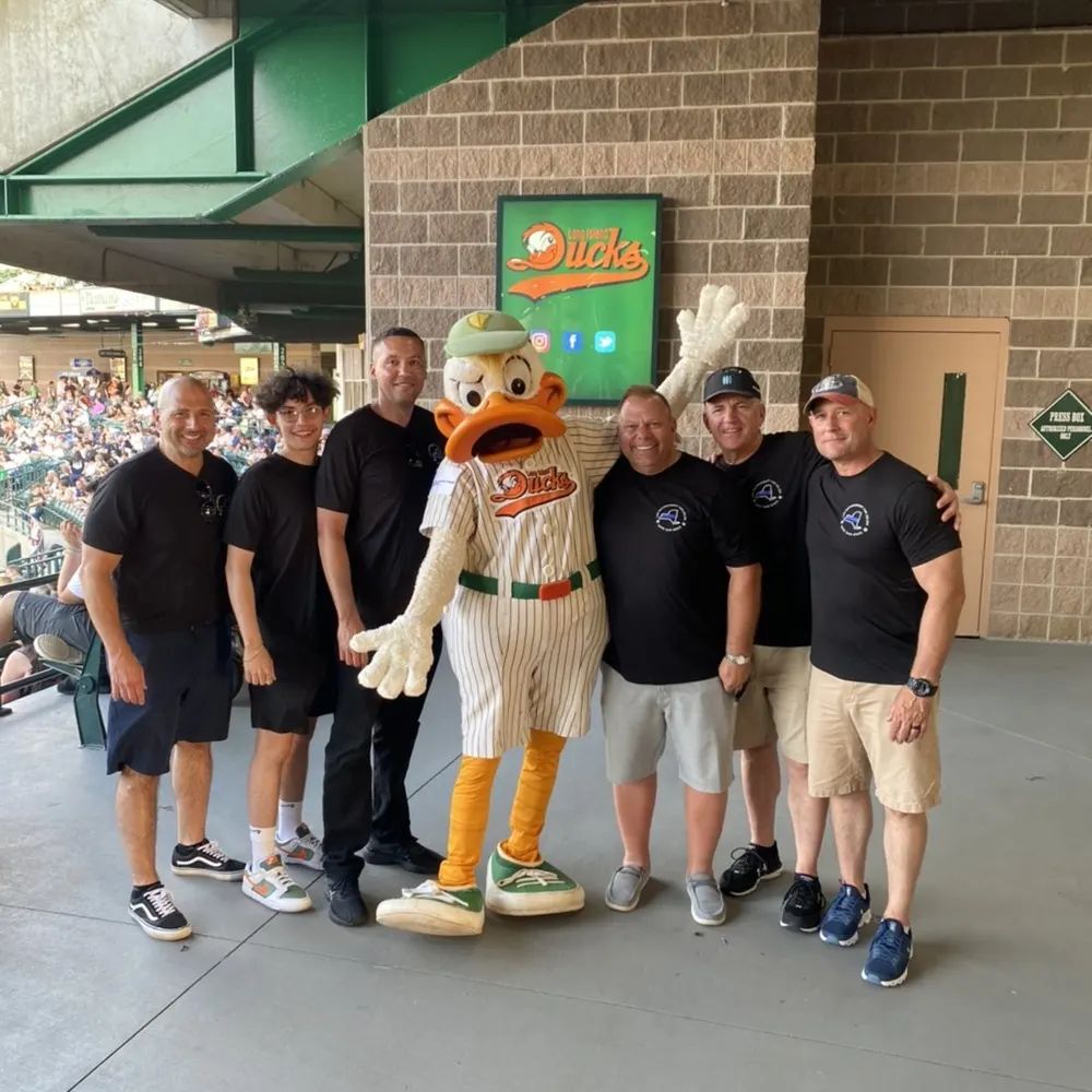 A group of men are posing for a picture with a duck mascot