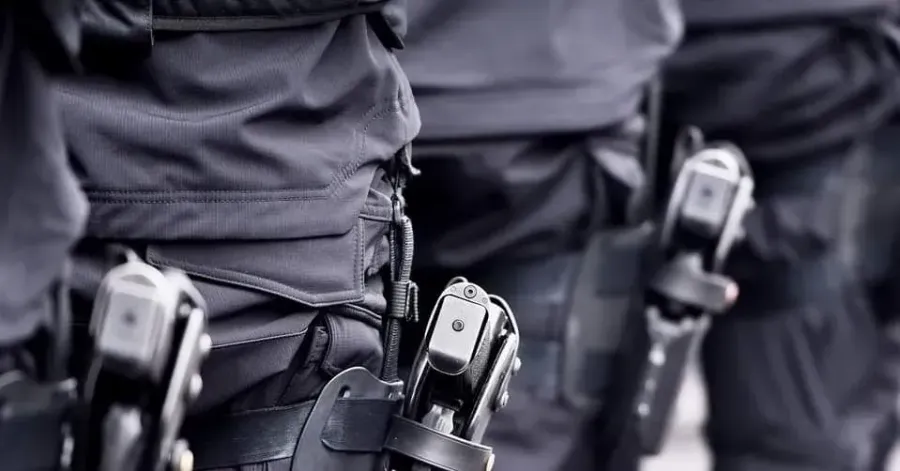 Close-up of tactical gear worn by a group of officers, showing holstered firearms attached to their utility belts.