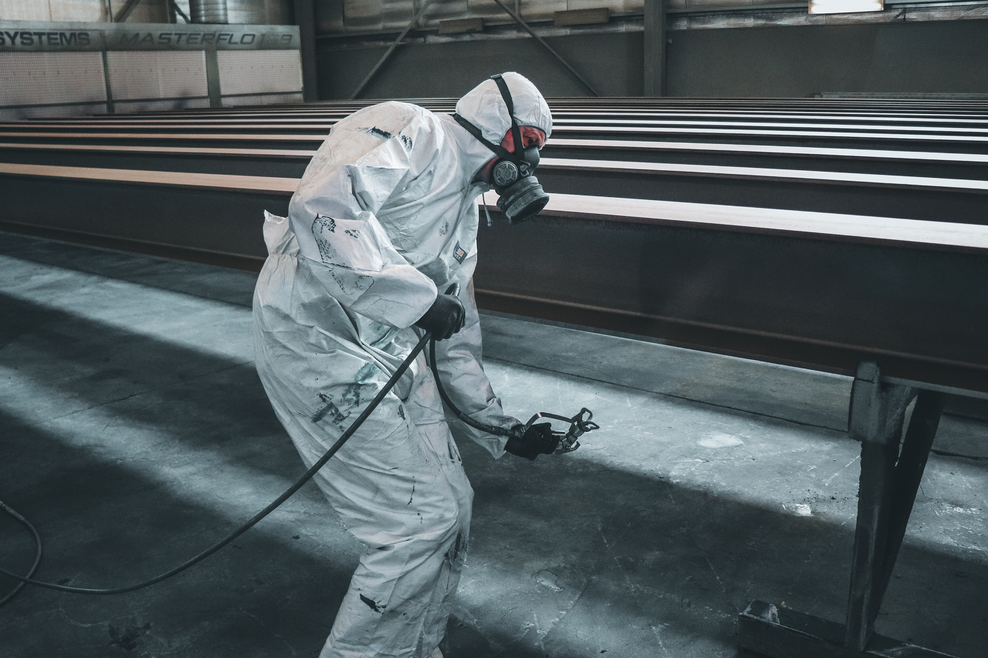 Worker in White Protective Suit Spray-painting a Metal Structure — Vent Doors Australia in Bohle, QLD