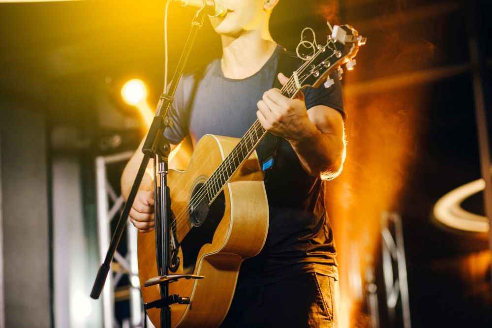 A Man Is Playing An Acoustic Guitar And Singing Into A Microphone On A Stage — Pacific Palms Bowling Club In Smiths Lake, NSW