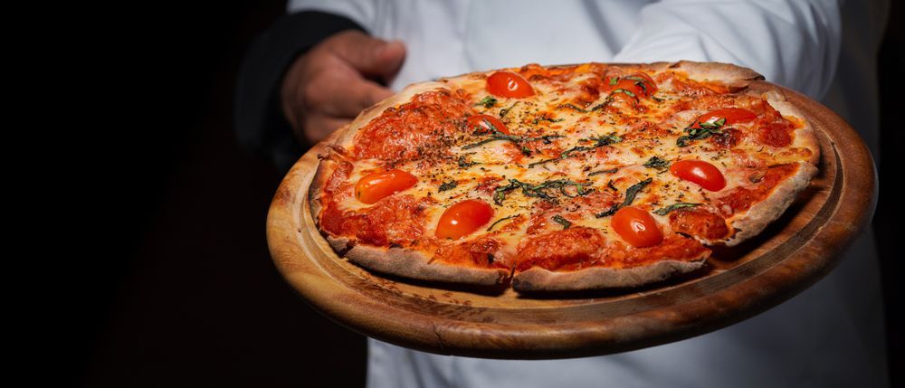 A Man Is Holding A Pizza On A Wooden Cutting Board — Pacific Palms Bowling Club In Smiths Lake, NSW