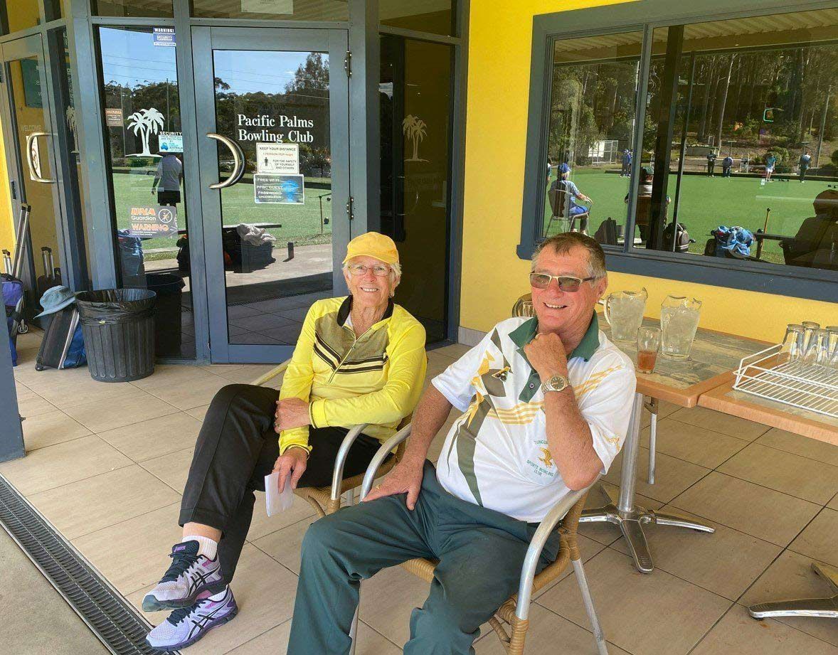 A Man And A Woman Are Sitting In Chairs Outside Of A Building — Pacific Palms Bowling Club In Smiths Lake, NSW