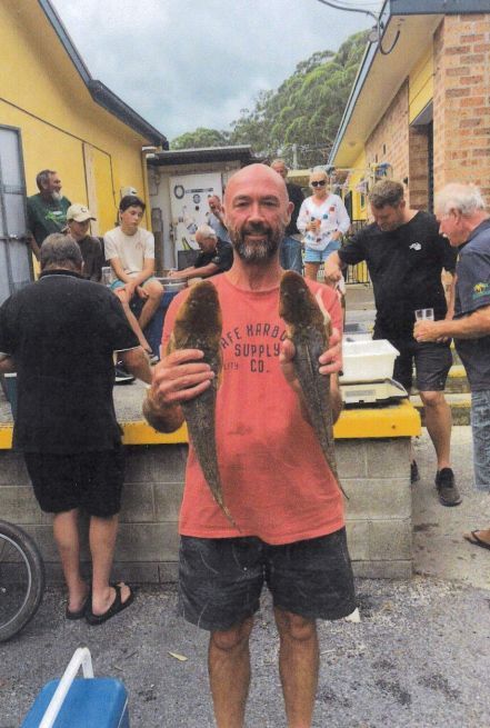 A Man In A Red Shirt Is Holding Two Fish — Pacific Palms Bowling Club In Smiths Lake, NSW