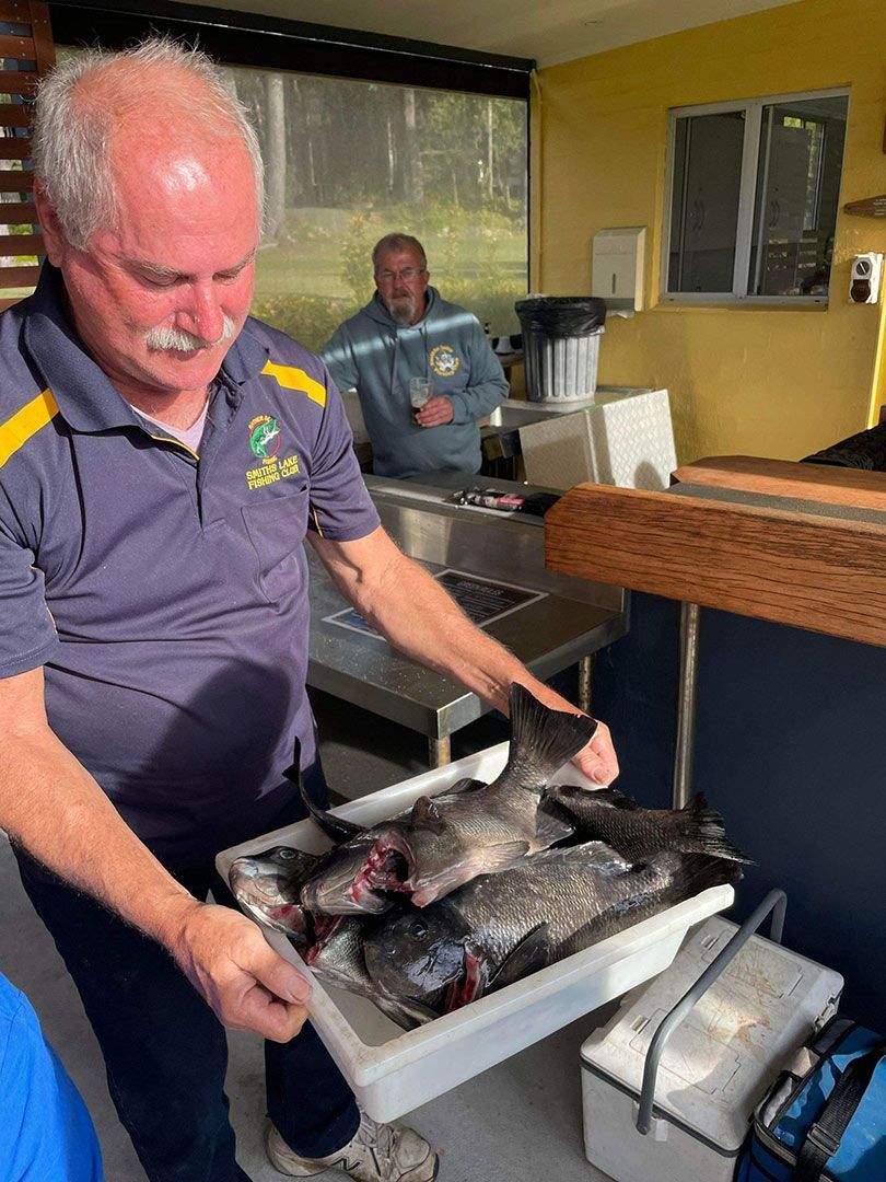 A Man Is Holding A Tray Of Fish In A Kitchen — Pacific Palms Bowling Club In Smiths Lake, NSW
