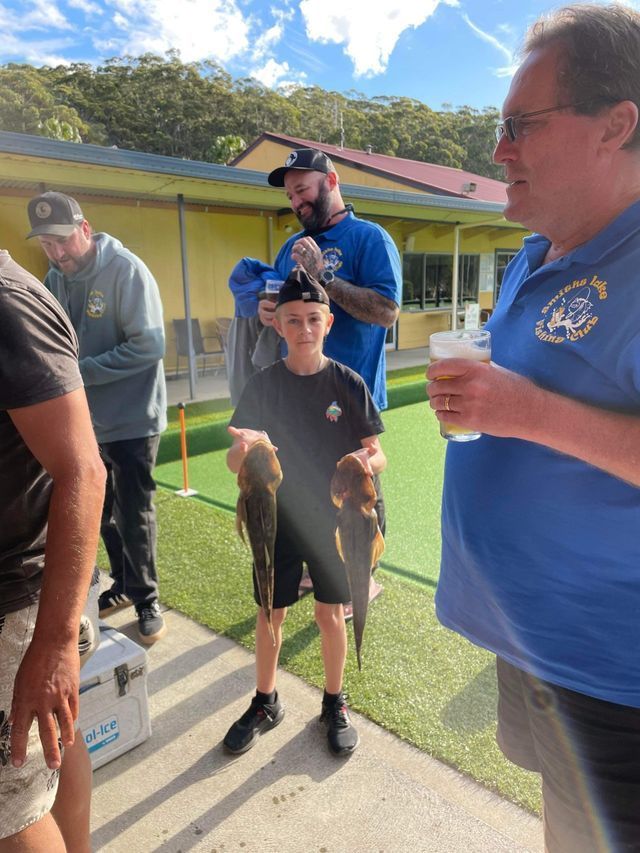 A Group Of Men Are Standing Around A Boy Holding A Fish — Pacific Palms Bowling Club In Smiths Lake, NSW