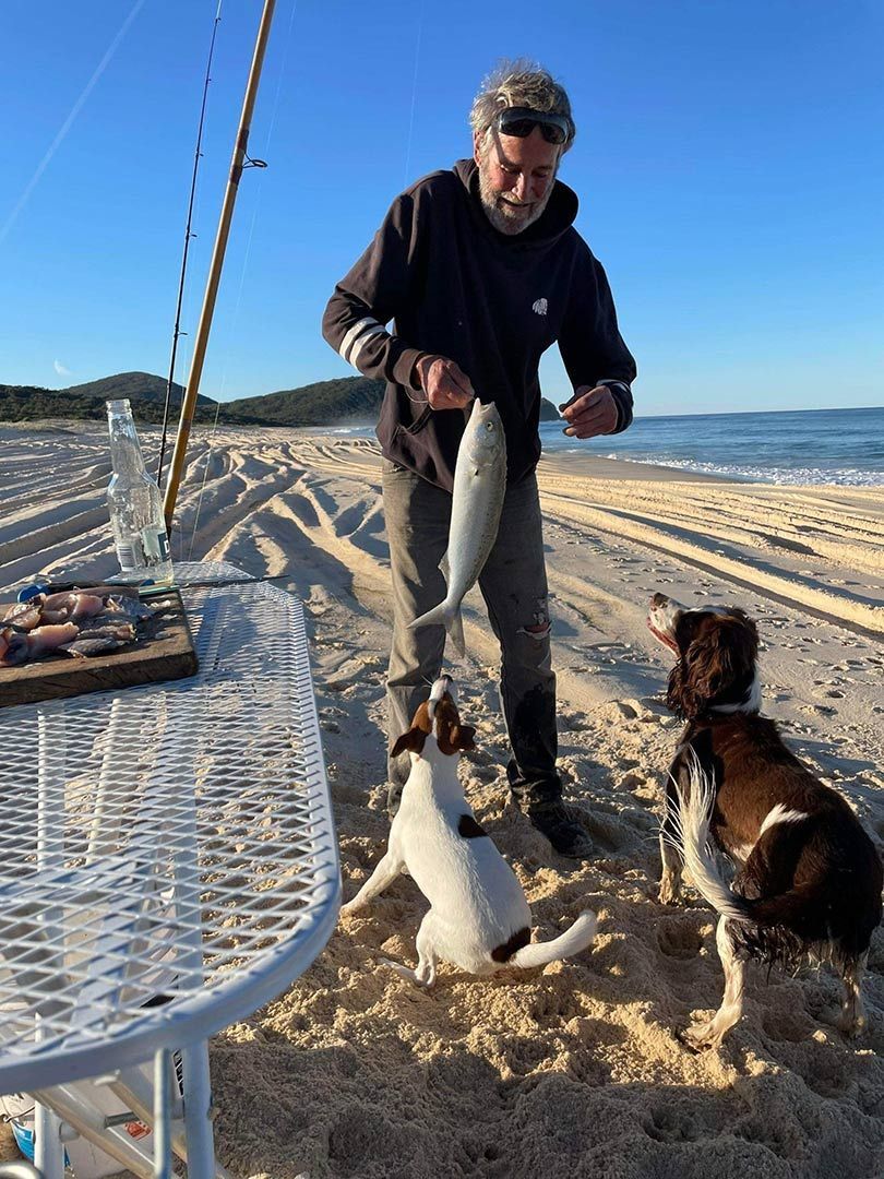 A Man And A Dog Are Standing On A Beach Holding Fish — Pacific Palms Bowling Club In Smiths Lake, NSW