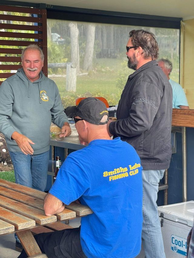 A Group Of Men Are Sitting At A Picnic Table Talking To Each Other — Pacific Palms Bowling Club In Smiths Lake, NSW
