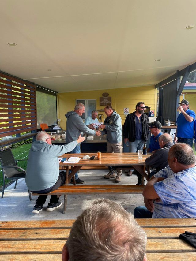 A Group Of Men Are Sitting At Picnic Tables And Shaking Hands — Pacific Palms Bowling Club In Smiths Lake, NSW