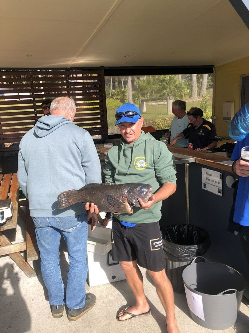 A Man Is Holding A Large Fish In His Hands In Front Of A Group Of People — Pacific Palms Bowling Club In Smiths Lake, NSW