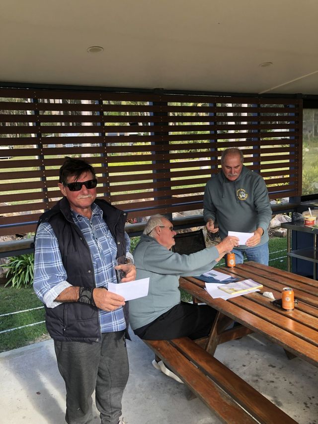 Three Men Are Standing Around A Wooden Picnic Table — Pacific Palms Bowling Club In Smiths Lake, NSW