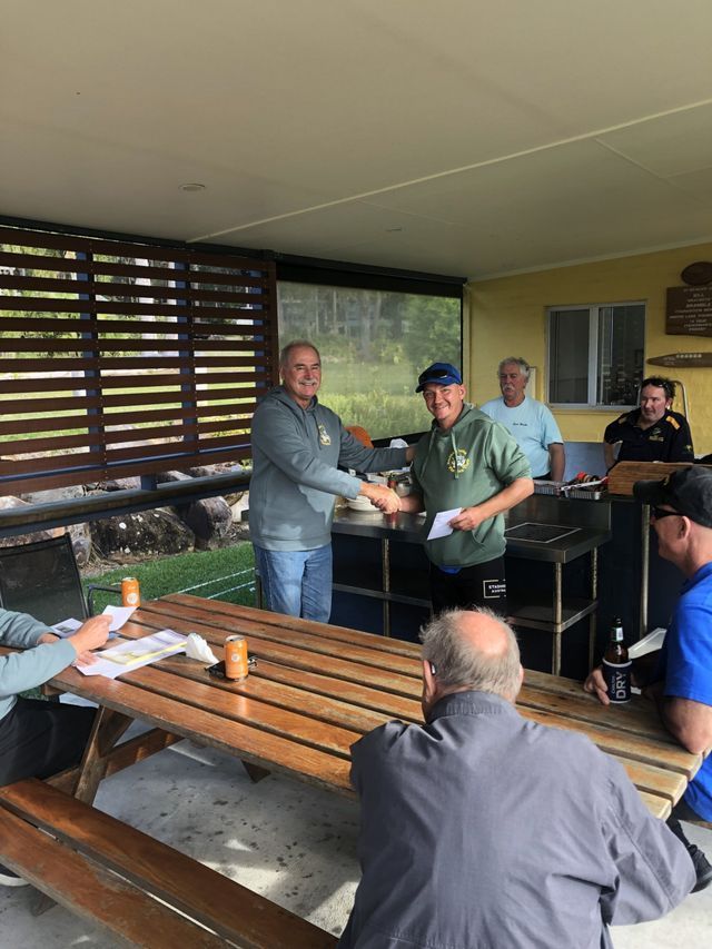 A Group Of Men Are Sitting At A Picnic Table And Shaking Hands — Pacific Palms Bowling Club In Smiths Lake, NSW