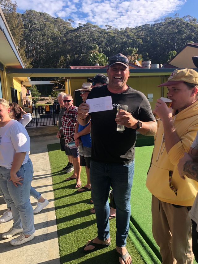 A Man Is Standing In Front Of A Group Of People Holding A Glass And A Piece Of Paper — Pacific Palms Bowling Club In Smiths Lake, NSW