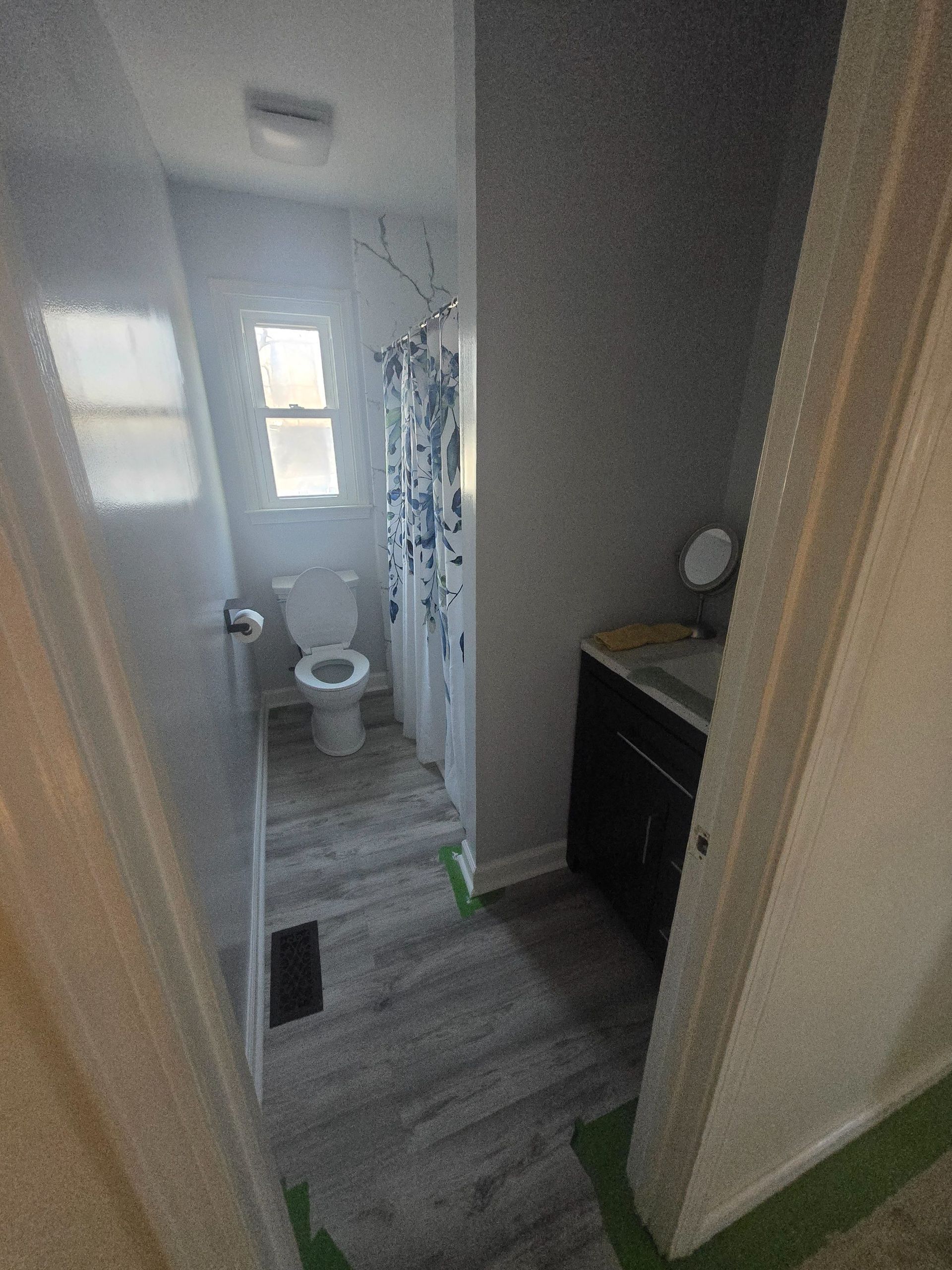 A bathroom featuring a toilet, a shower with a patterned curtain, and a dark wood vanity with a white countertop.