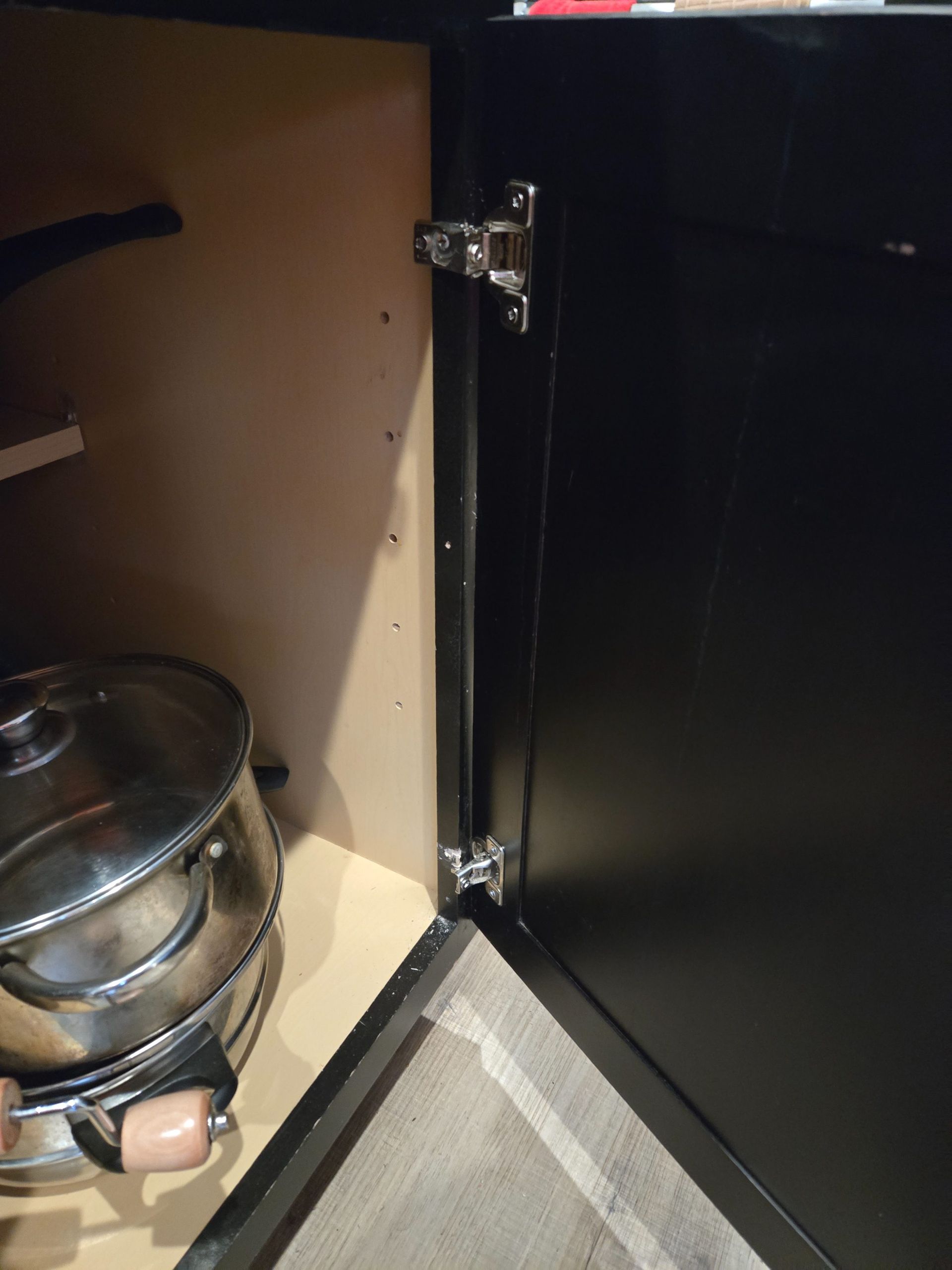 Open black cabinet door revealing a stack of stainless steel pots with glass lids inside.
